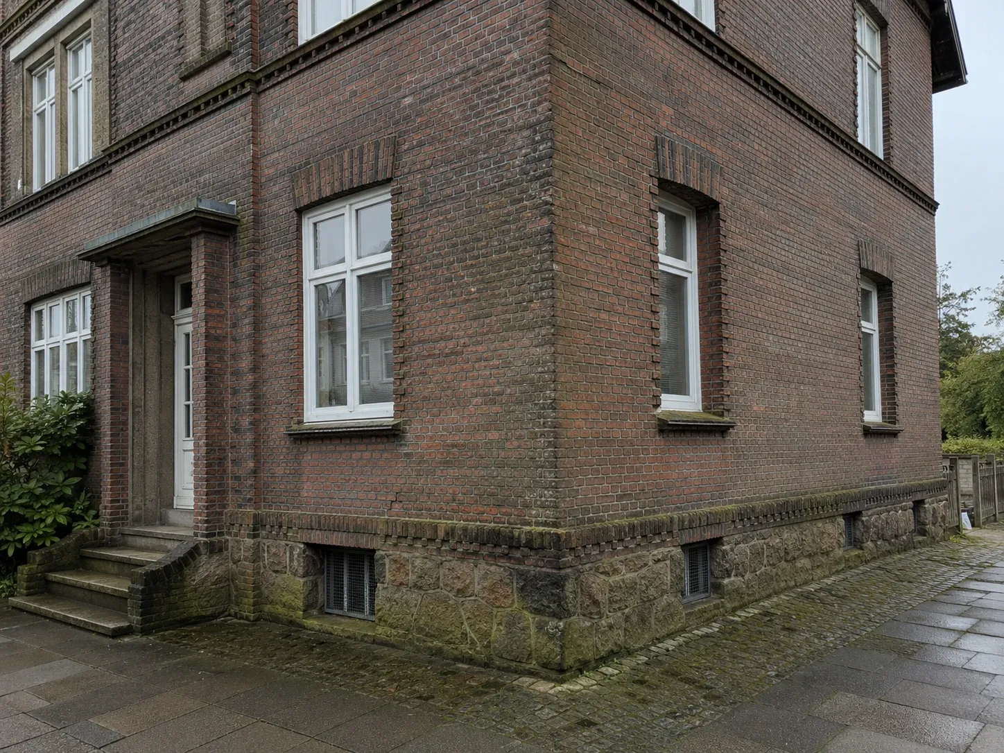 Rotklinkerfassade eines Hamburger Altbaus vor der Reinigung, Ziegel vergraut und Natursteinsockel bemoost