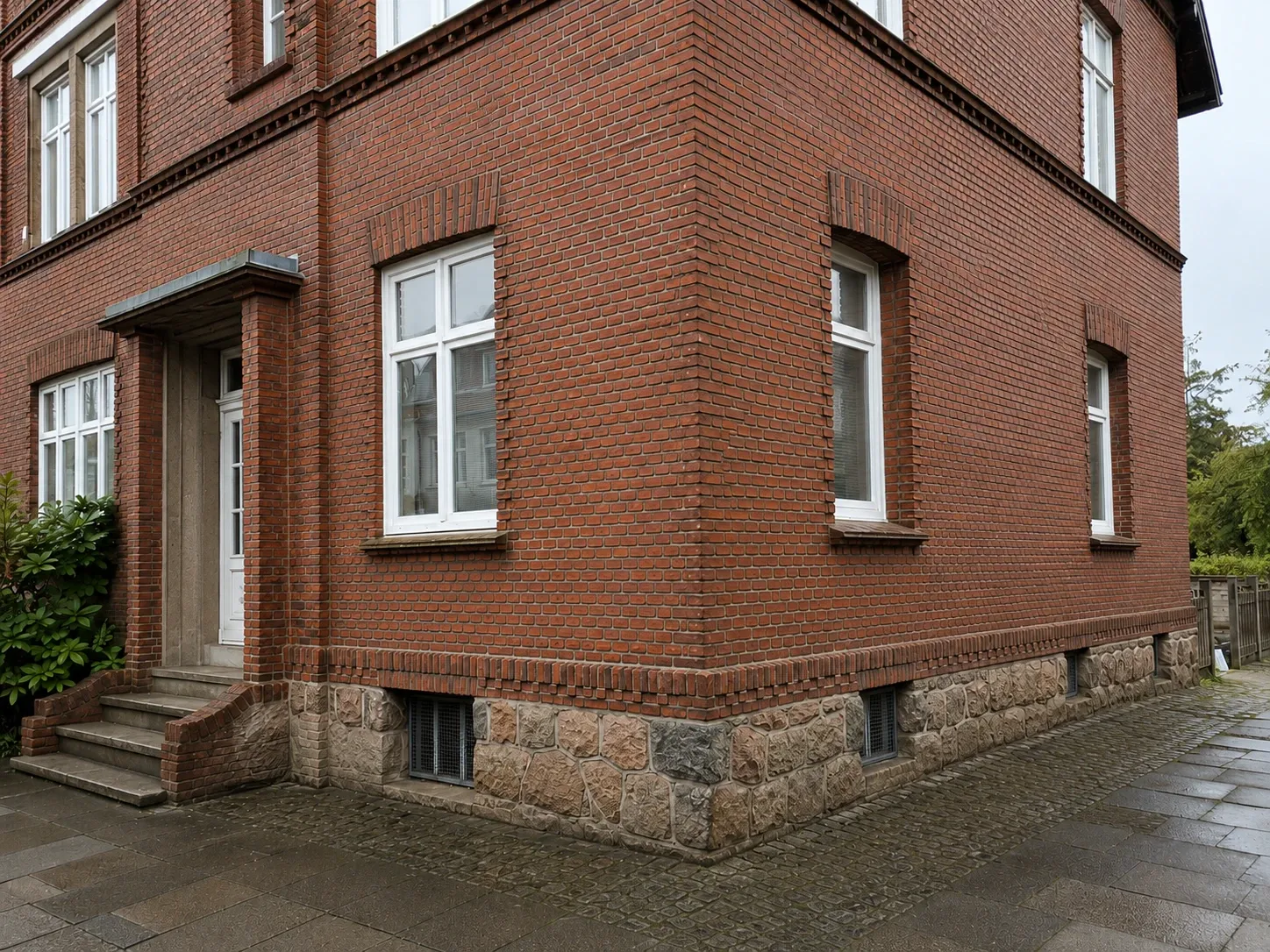 Dieselbe Rotklinkerfassade nach der Reinigung, kräftig roter Ziegel und heller Natursteinsockel