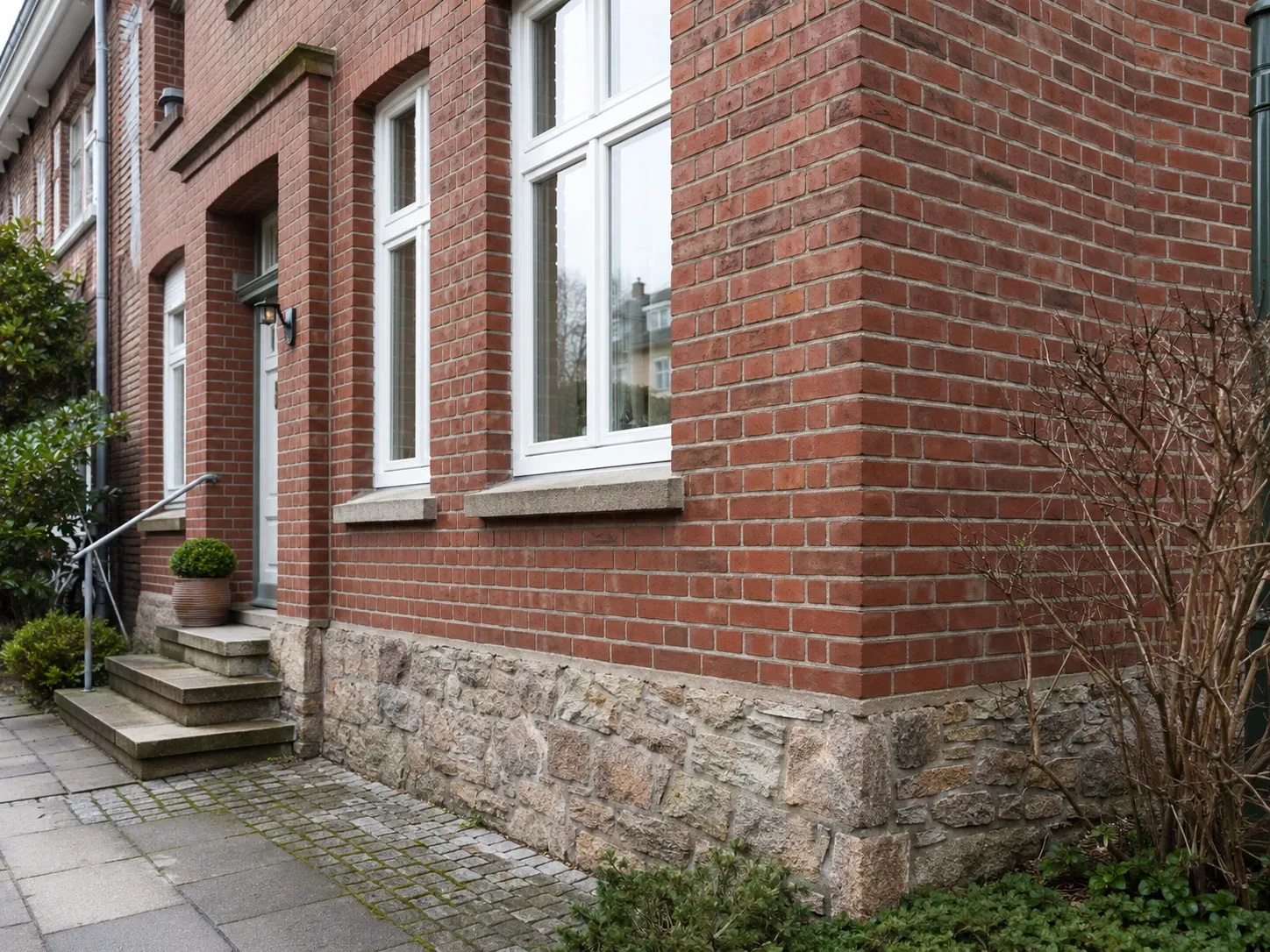 Sauberer Rotklinker mit Natursteinsockel und weißen Fenstern an einem Hamburger Altbau